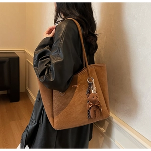 Detail of brown suede tote bag with gold logo and plush bear charm on model's shoulder