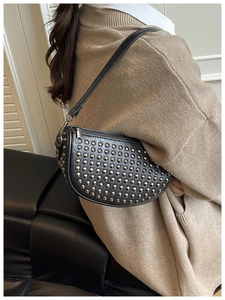 Model showing a black leather crescent shoulder bag with metallic silver rivets in detail