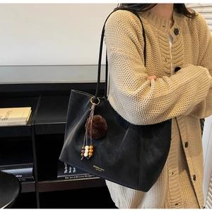 Detail of black matte leather tote bag with a plush charm and colorful wooden beads