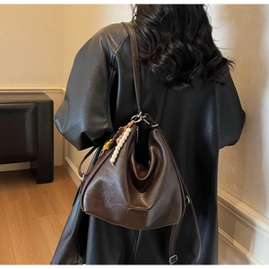 Detail of dark brown leather hobo bag with colorful bead charm on a model in black leather jacket