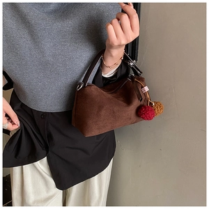 Détail du sac boston en daim marron foncé avec pompons colorés et rubans contrastés