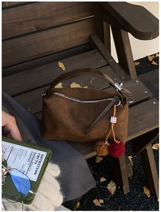 Détail du sac à main en daim marron avec pompon en peluche sur un banc d'automne