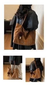 Détail d'un grand sac cabas en daim marron avec un charme en peluche et de fines bandoulières