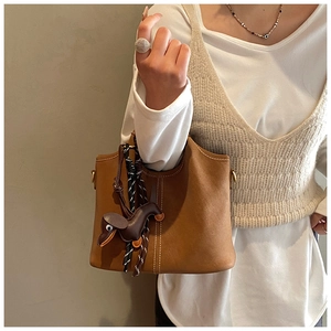 Detail einer braunen Leder-Eimertasche mit Kontrastnähten und Hunde-Taschenanhänger