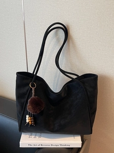 Borsa tote nera minimalista con ciondolo a pompon in pelliccia su libri bianchi