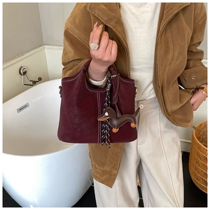 Detail der dunkelroten Beuteltasche mit weißen Nähten und Dackel-Anhänger