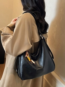 Chic black half-moon hobo bag with colorful wooden beads on a stylish beige trench coat