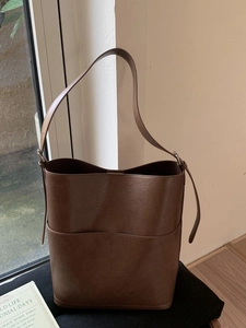 Sac seau marron en similicuir avec poche avant et bandoulière réglable sur canapé