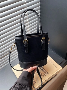 Vintage black bucket bag with textured contrast leather and gold hardware on retro background