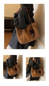 Detail of a large brown matte leather tote bag with a decorative faux fur pompom charm