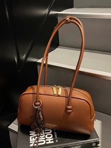 Brown litchi grain leather bowling bag with slim handles and golden zippers on books