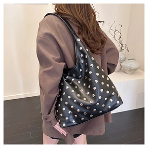 Détail du sac hobo noir à rivets argentés porté par un mannequin en manteau