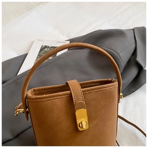 Close-up of brown bucket bag showing matte texture and metallic buckle on a white background
