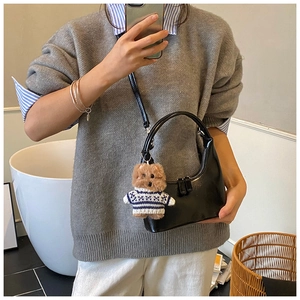 Détail d'un sac à bandoulière noir brillant en demi-lune avec breloque ours sur modèle