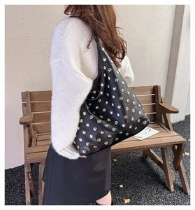 Détail d'un sac hobo en cuir noir avec rivets argentés porté par un mannequin en extérieur