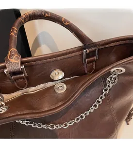 Dettaglio di fibbia magnetica, catena argento e manici monogramma su borsa in pelle scura