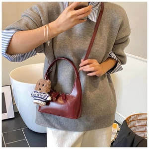 Détail d'un sac à main rouge vin brillant avec un charmant petit pendentif ours brun
