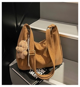 Sac fourre-tout marron avec charme d'ourson posé sur un escalier gris moderne