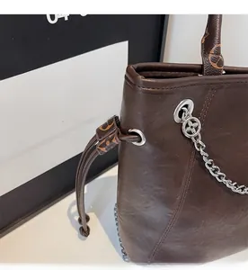 Dettaglio della borsa tote in pelle caffè con ciondolo a catena e chiusura monogram
