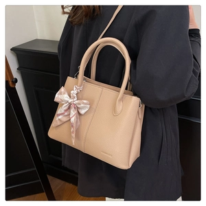 Detail of beige lychee leather bucket bag with decorative silk scarf and thin strap