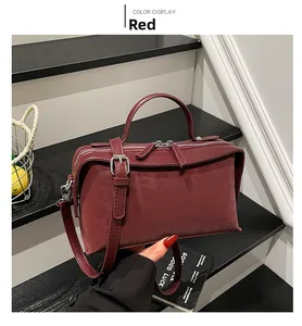 Close-up of matte red leather shoulder bag with dual zippers and adjustable strap on stairs