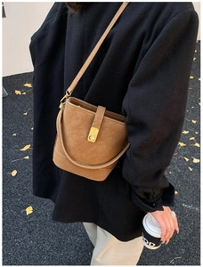 Brown suede bucket bag with gold clasp shown on model against autumn gingko leaves