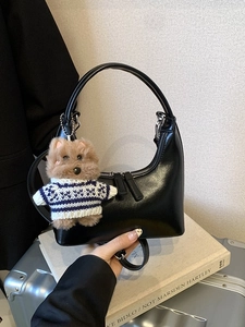Sac à bandoulière rétro noir en cuir avec breloque ours, posé sur une valise argentée