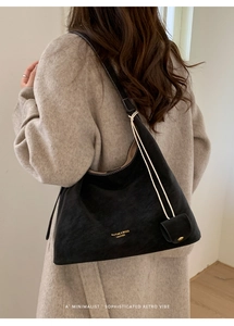 Detail of a large black leather tote bag with gold logo and small charm on a model