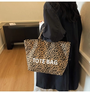 Close-up of leopard print canvas tote bag with white text held by a model in a cozy room