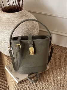 Retro dark green bucket bag with gold buckle and adjustable strap on white book
