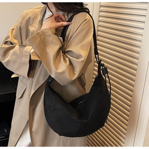 Minimalist black suede hobo bag with drawstring detail worn with a trench coat