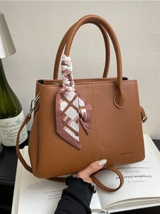 Brown lychee leather bucket bag with silk scarf and logo detail on elegant background