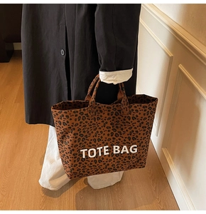 Detail of leopard print canvas tote bag with white TOTE BAG text carried by model
