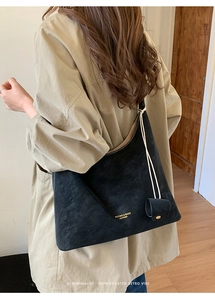 Detailed view of black suede tote bag with gold lettering on a khaki coat model