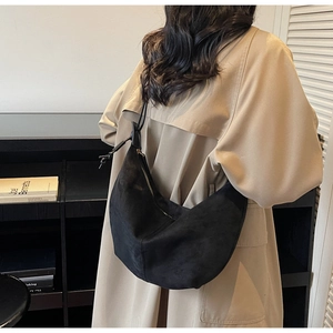 Detail of large black suede hobo bag with zip closure worn by a model in a library