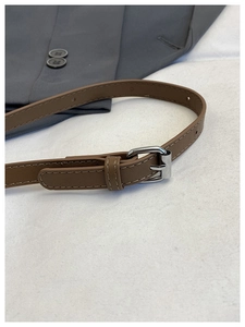 Close-up of a brown leather belt with silver needle buckle on a gray suit background