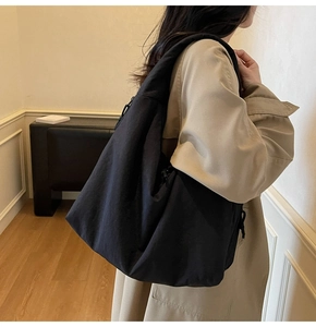 Close-up of a large black canvas tote bag styled with a minimalist trench coat
