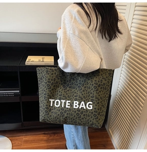 Detail of large leopard print tote bag in dark green canvas worn by a model