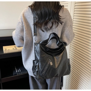 Detail of black leather tote bag with wide shoulder strap and side storage pocket