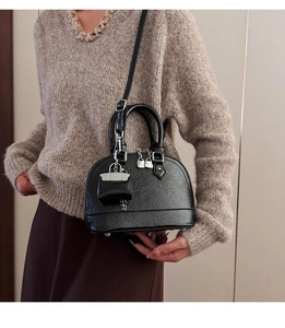 Détail d'un sac à main noir en forme de coquillage porté avec un pull beige élégant