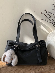 Large black suede tote bag with plush bunny pendant on a rustic wooden table background