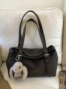 Brown suede tote bag with silver hardware and plush rabbit pendant on a beige sofa