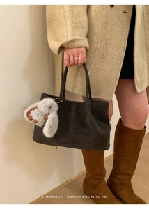 Detail of dark gray suede bucket bag with vertical stitching and plush bunny pendant