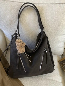 Large vintage brown faux leather tote bag with plush dog charm on beige sofa