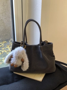 Dark grey matte suede bucket bag with plush bunny pendant on a black cushion