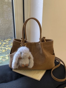 Brown suede bucket bag with plush rabbit charm displayed in a cozy autumn indoor setting