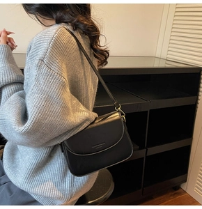 Close-up of black leather crossbody bag featuring a golden metal clasp and embossed logo