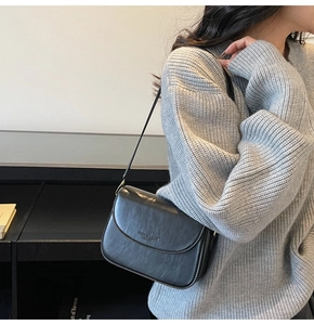 Detail of minimalist black leather crossbody bag with embossed lettering on textured fabric