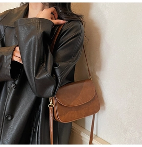 Detailed view of vintage brown leather crossbody bag with debossed fashion logo on a model