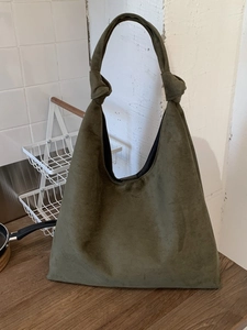 Vintage dark green suede tote bag with knotted strap on a wooden tabletop